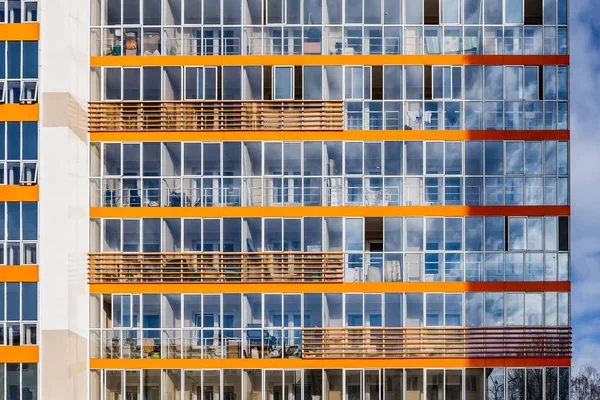 Um novo edifício moderno de dormitório estudantil no campus com muitas janelas com reflexos de céu azul com nuvens brancas. Textura horisontal de janelas azuis e decore laranja — Fotografia de Stock