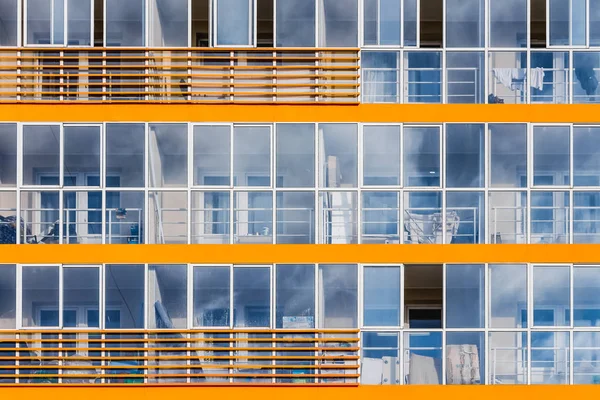 Un nouveau bâtiment moderne de dortoir étudiant sur le campus avec de nombreuses fenêtres avec des reflets de ciel bleu avec des nuages blancs. Texture horisontale des fenêtres bleues et décor orange — Photo