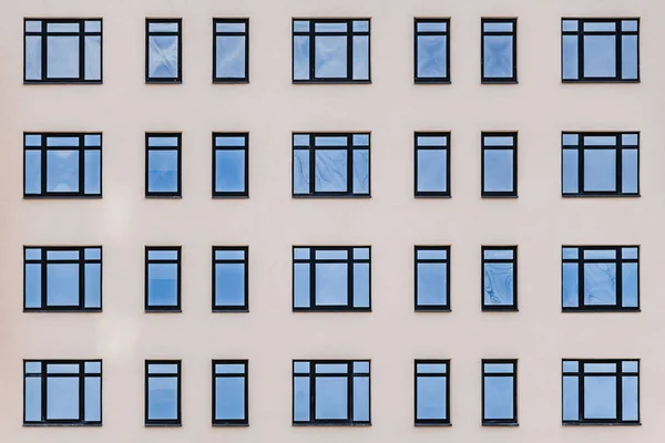 Una parte de una pared amarilla con ventanas azules con reflejos de cielo azul de un nuevo edificio moderno. Textura horizontal de las ventanas azules en una pared amarilla — Foto de Stock