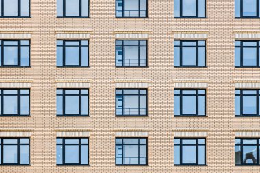 Mavi gökyüzü yansımaları ile mavi pencerelerin bir grup ile sarı tuğla duvarın bir parçası. Sarı duvardaki mavi pencerelerin yatay dokusu