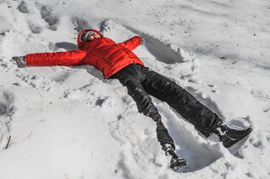 Kırmızı ceketli bir kadın ve kış parkında beyaz karda siyah pantolon. Bir kadın melek gibi karda yatıyor.