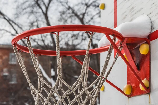 A beautiful red basketball hoop with white rope net and white snow on the childrens playground in the yard in winter — Stock Photo, Image