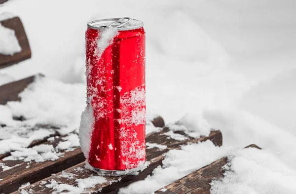 Otwarta czerwona błyszcząca jasna puszka z białym śniegiem na jego powierzchni z kluczem do chłodnych napojów bezalkoholowych na drewnianej ławce z białym śniegiem do chłodzenia jak w lodówce zimą — Zdjęcie stockowe