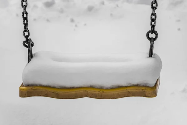 Huśtawka malowana żółtą farbą z czarnym metalowym łańcuszkami na placu zabaw dla dzieci na dziedzińcu zimą — Zdjęcie stockowe