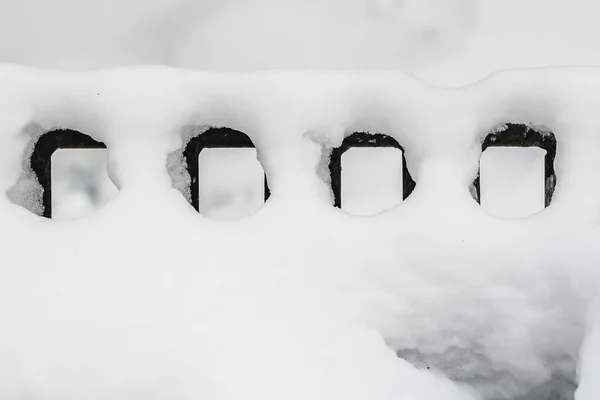 Zaspie śniegu białym światłem słońca i bokeh na black metalu kute ogrodzenia na niewyraźne tło w parku w zimie — Zdjęcie stockowe