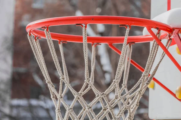冬の庭の子供の遊び場に白いロープのネットと白い雪の美しい赤いバスケットボールのフープ — ストック写真