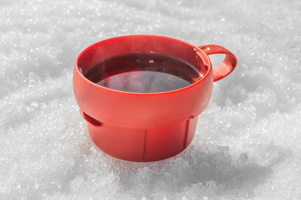 Красная пластиковая кружка с черным горячим чаем с паром на белом фоне снега зимой для пикника — стоковое фото