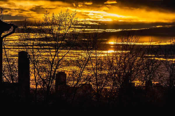 Svarta silhuetter av träd utan löv och byggnader och svarta trådar är på en orange himmel bakgrund med röda gula moln och solnedgång sön — Stockfoto