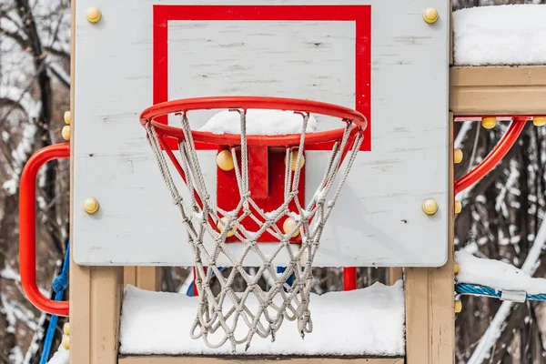 Um lindo aro de basquete vermelho com rede de corda branca e neve branca no parque infantil no quintal no inverno — Fotografia de Stock