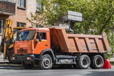 Turuncu kamyon ve sarı ekskavatör yaz aylarında bir şehirde asfalt yol onarımı için iş