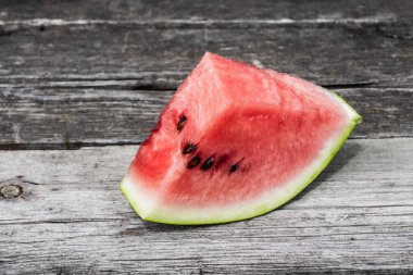 Bir yaz bahçesinde kaba gri eski ahşap yüzey üzerinde parlak sulu kırmızı tatlı karpuz üçgen dilim