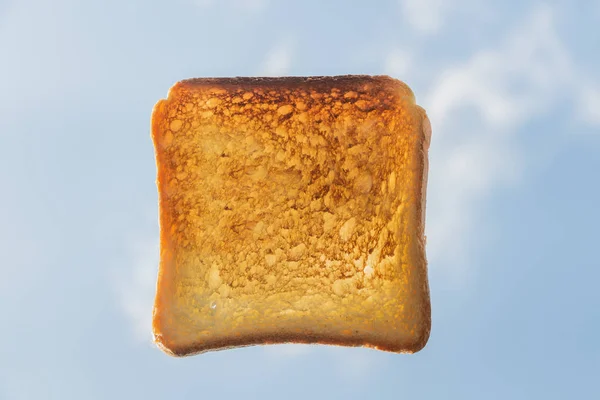 Один квадратный румяный кусок хлеба для тостов на голубом небе на фоне белых облаков — стоковое фото