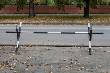 Siyah ve beyaz metal çit sonbaharda sarı yaprakları ile yol kenarında araba geçişini yasaklamak için duruyor