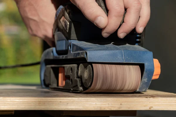 Один чоловік робить обробку деревини за допомогою синьої шліфувальної машини — стокове фото