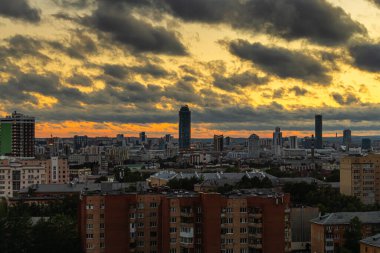 Şehir, turuncu ve sarı günbatımıyla gökyüzü arka planında.