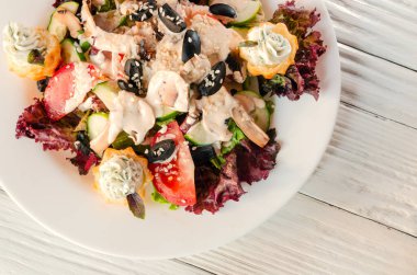 Tahta bir arka planda beyaz bir tabakta sebze salatası.