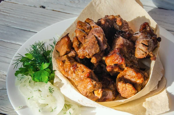 Grilled meat laid out on a plate in pita bread with herbs and fresh onions.