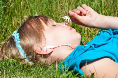 Genç beyaz kız müzik dinlerken beyaz papatya kokulu çim üzerinde yalan