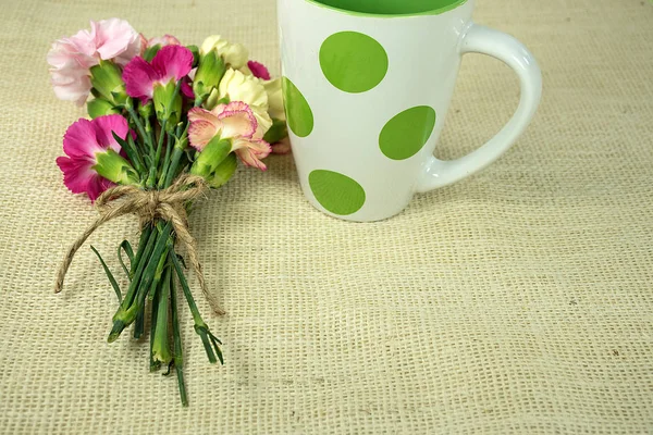 カーネーションの花束は 黄麻布の文字列と水玉のマグカップと結ばれる — ストック写真