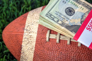 close up of wrapped money stack on used football with green grass background clipart