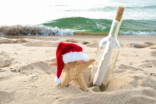 ホリデイ サンタ帽子とボトルのメッセージと砂浜にヒトデ — ストック写真