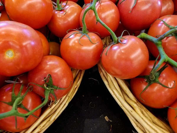 close up of red ripe tomatoes with vine in wicker basket the market