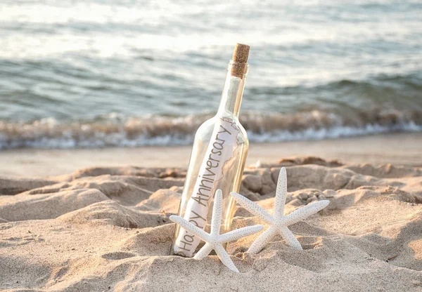一对白色海星在沙滩沙滩上 在海边的瓶子里带着快乐的周年信息 — 图库照片