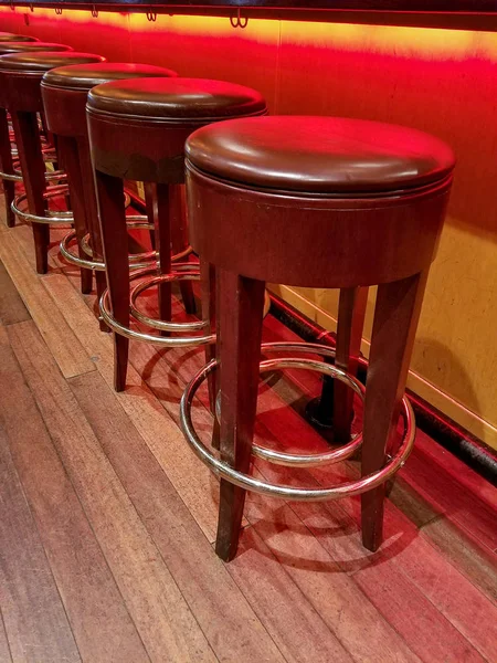 row of retro bar stools on wood floor under bar counter with red neon lighting