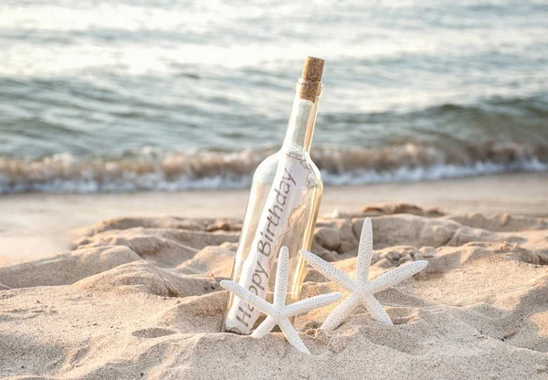 一对白色海星与快乐的生日消息在沙滩上的沙滩上的瓶子 — 图库照片