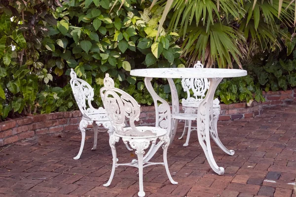 在热带花园的砖天井上设置的白色锻铁桌子和椅子 — 图库照片