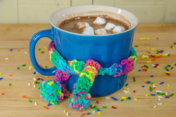 热巧克力饮料与五颜六色的针织围巾绑在木桌上的蓝色杯子和洒 — 图库照片