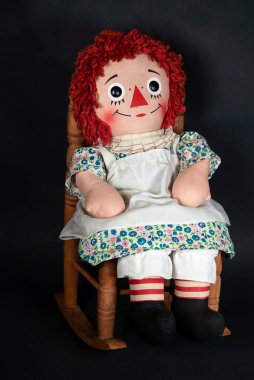 ahşap sallanan sandalyede oturan beyaz apron ile eski bez bebek