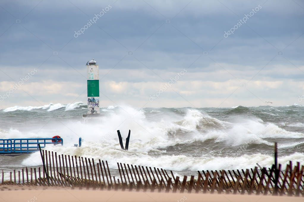 high waves on stormy Lake Michigan with green and white channel marker and beach fence