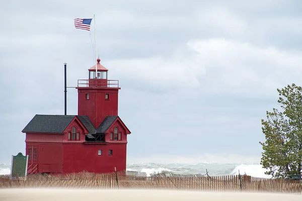 Red Michigan lighthouse on Lake Michigan with beach fence and high seas in wind storm