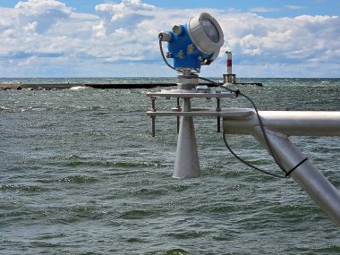 Elektronik ekipmanlara sahip metal bir yapı okyanusun üzerine monte edilir ve arka planda bir delici işaret ışığı görünür. 