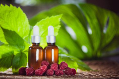 Şişe ile ahududu yağı, taze çilek ve ahududu yaprakları doğal yeşil bir arka plan üzerinde