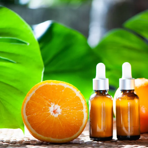 Portakal yağı, taze meyve bütün ve doğal tropikal arka plan üzerinde yarım şişe.