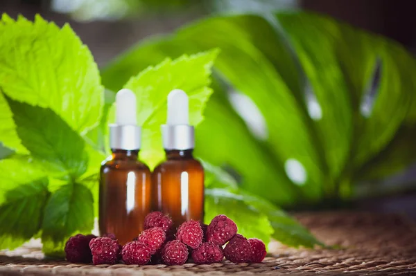 Şişe ile ahududu yağı, taze çilek ve ahududu yaprakları doğal yeşil bir arka plan üzerinde
