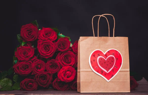 large bunch of red roses and a gift bag with a heart. The concept of a gift for Valentine\'s Day, love, wedding, date
