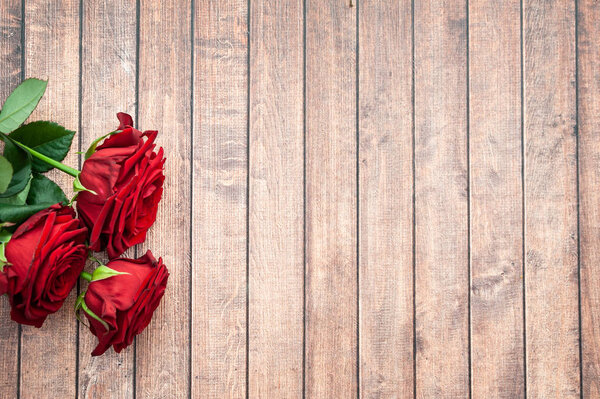 Three roses on a wooden background, space for text