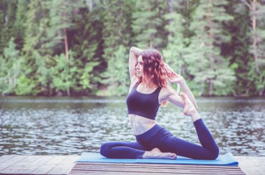 Gölde yoga pozu alan güzel kız. Eka Pada Rajakapotasa