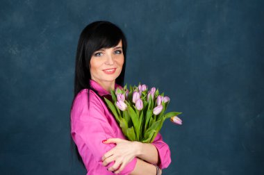 Güzel bir kız, parlak pembe gömlekli esmer, bir buket lale çiçeğiyle, kameraya bakıyor, yazın teması, bahar. 