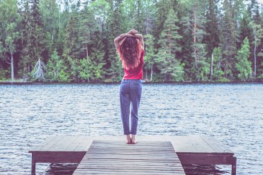 Genç kız güzel bir gölün rıhtımında duruyor, kollarını kaldır. Yaz havası, doğanın güzelliği, yazın neşesi..