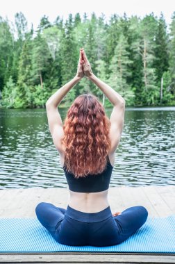 Güzel bir gölün rıhtımında genç bir yogi kızının poz verdiği nilüfer çiçeğiyle yoga meditasyonu. Sağlıklı yaşam ve doğal denge kavramı 
