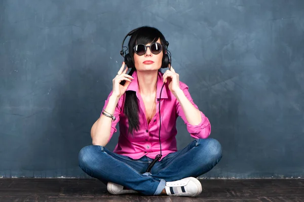 Trendy beautiful girl brunette DJ in headphones, listens to and records music, smiles, studio portrait on a monochrome blue, trendy shabby background, space for text. Theme of music