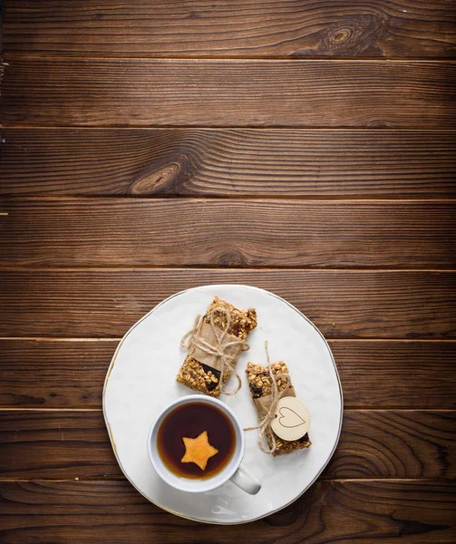 Hausgemachte Müsli-Haferflocken-Energieriegel und eine Tasse Tee auf weißem Teller, gesunder Snack, Kopierraum auf dem Holztisch — Stockfoto