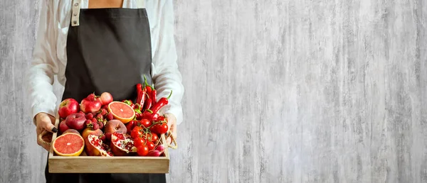 Girl holds wooden tray with fresh red vegetables and fruits on grey background. Healthy eating vegetarian concept. — Stock Photo, Image