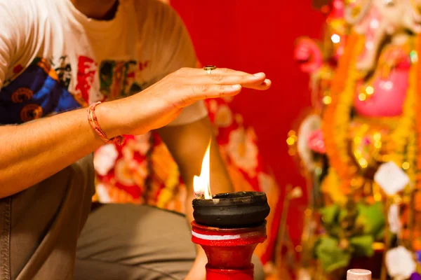 a hand taking heat of the flame as blessing from a lit clay lamp on top of a clay stand or worship idol durgapuja india diwali