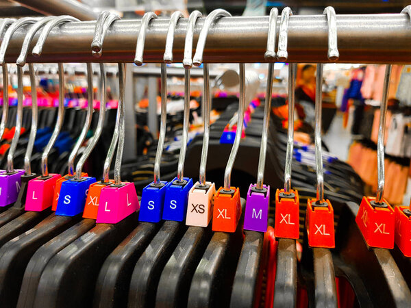 Вешалка разного размера с ярлыками XL L M XS t рубашки, выставленные в магазине на продажу
