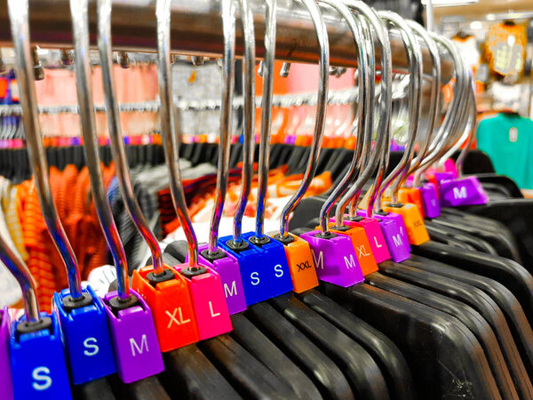 Вешалка разного размера с ярлыками XL L M XS t рубашки, выставленные в магазине на продажу
